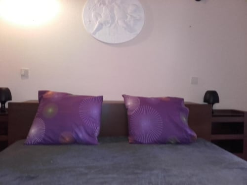 Quarto do apartamento Albufeira Inn com almofadas decorativas roxas na cama e ventilador de teto branco