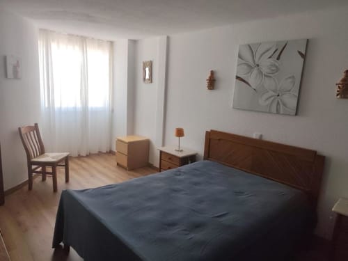 Quarto luminoso na Albufeira Inn com cama de madeira, cadeira e obra de arte moderna no apartamento Santa Eulália