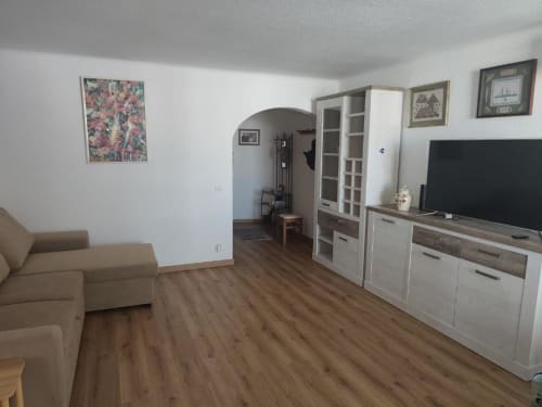 Sala de estar espaçosa no apartamento Albufeira Inn com sofá bege, TV de ecrã plano, móveis brancos, piso em madeira e entrada