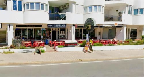 Terraço beira-mar do Albufeira Inn com cadeiras vermelhas, bares e edifício de apartamentos brancos em Albufeira, Portugal