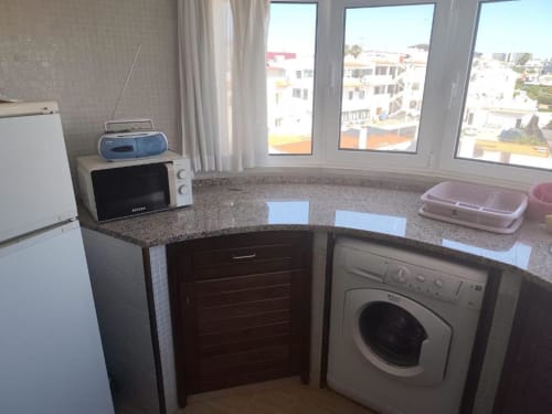 Cozinha moderna com máquina de lavar, micro-ondas e bancadas em granito com vista para Albufeira no apartamento Edifício Coral