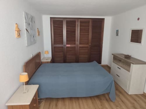 Quarto da Albufeira Inn com cama azul, móveis de madeira e guarda-roupa com portas basculantes
