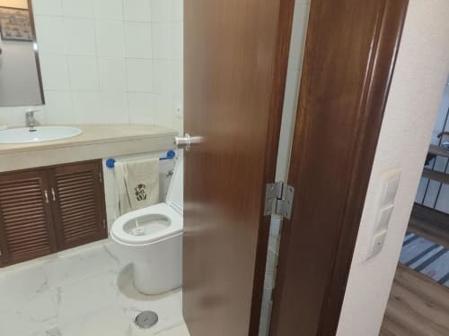 Casa de banho moderna na Albufeira Inn com lavatório branco, móvel de madeira, sanita e cabine de duche no apartamento de Santa Eulália