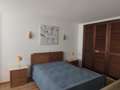Quarto da Albufeira Inn com móveis de madeira, cama azul, portas para terraço e arte floral nas paredes em Santa Eulália
