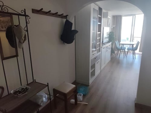 Entrada do apartamento Albufeira Inn com bengaleiro, banco em madeira, guarda-roupa e vista para a sala de estar com varanda