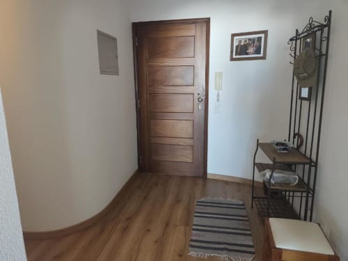 Entrada do apartamento Albufeira Inn com porta de madeira, piso de madeira, tapete listrado e cabideiro metálico