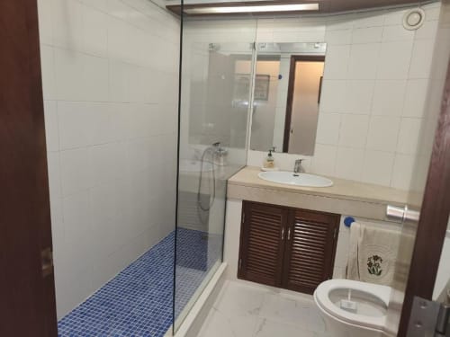 Casa de banho moderna no Albufeira Inn com duche em vidro, piso em azulejos azuis e móvel lavatório em madeira escura