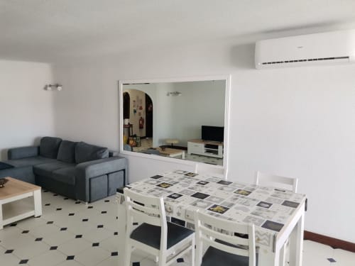 Área de estar moderna e aberta na Albufeira Inn com mesa de jantar, sofá escuro e parede espelhada no apartamento T1