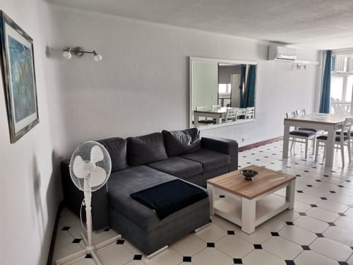 Sala de estar moderna no Albufeira Inn com sofá preto, mesa de café em madeira e área de refeições em apartamento luminoso com azulejos