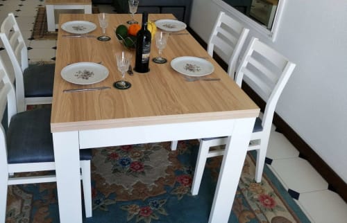 Mesa de jantar posta para quatro pessoas na Albufeira Inn com cadeiras brancas, talheres, garrafa de vinho e arranjo de frutas frescas.