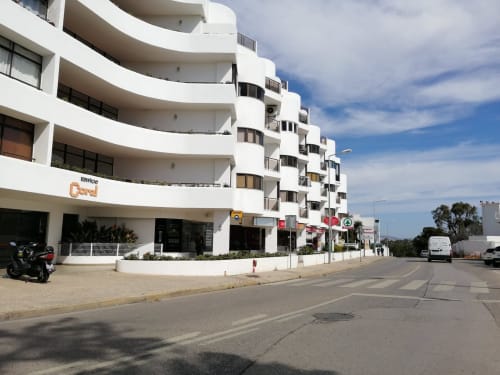 Edifício curvo branco em Albufeira com lojas no piso térreo, varandas e vista da rua