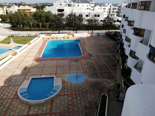 Área de piscina do Albufeira Inn com piscinas azuis, pátio em tijolos vermelhos, edifício branco e paisagem envolvente