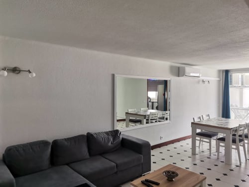 Sofá preto e mesa de madeira em sala de estar moderna do apartamento Albufeira Inn, com espaço de refeição visível pela janela