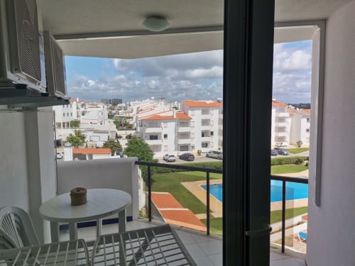 Varanda do apartamento em Albufeira com vista para piscina e pátio, edifícios brancos com telhados laranja próximos