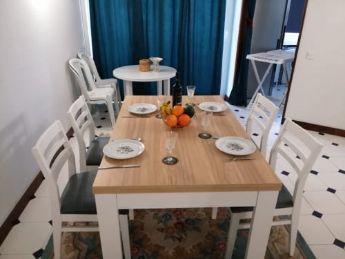 Sala de refeições do Albufeira Inn com mesa de madeira, cadeiras brancas, arranjo de mesa e cortinas azul-turquesa