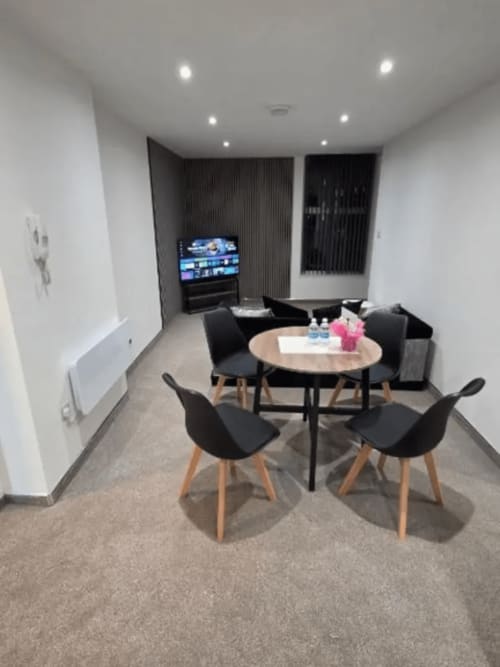 Modern lounge at JS Apartments Blackburn with round table, black chairs, TV, and comfortable seating area