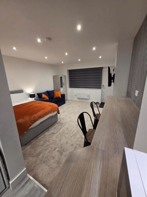 Modern studio apartment at JS Apartments Collection, Blackburn featuring bed with orange bedding, blue sofa, and wood