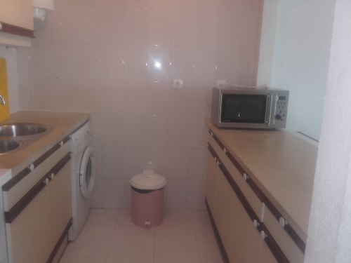 Cozinha compacta do apartamento Albufeira Inn com micro-ondas, fogão, máquina de lavar e armários bege