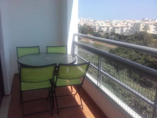 Varanda luminosa com cadeiras de refeição verdes, mesa redonda e vistas panorâmicas dos edifícios e litoral de Albufeira