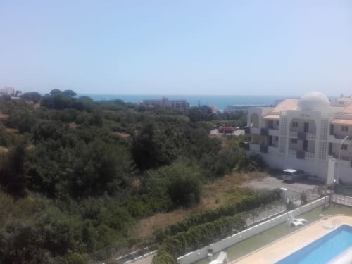 Vista da varanda do apartamento em Albufeira com piscina, oliveiras, edifícios costeiros e o Mar Mediterrâneo ao fundo