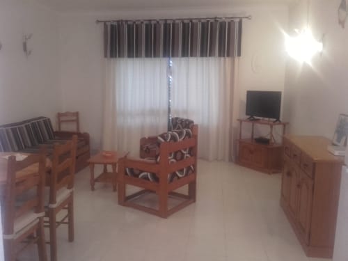 Sala de estar com móveis em madeira, TV e vista para o oceano no apartamento Albufeira Inn em Portugal