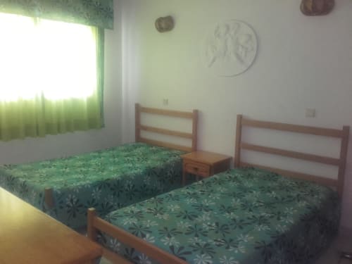 Quarto luminoso em apartamento em Albufeira com duas camas de solteiro, roupa de cama com padrão verde, estruturas de madeira e janela com verde