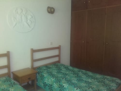 Quarto do apartamento em Albufeira com cama de madeira, roupa de cama com padrão verde, criado e guarda-roupa no Edifício