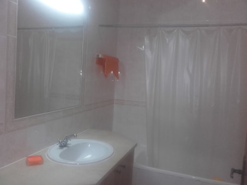 Banheiro limpo com pia redonda, espelho e cortina de chuveiro no apartamento Albufeira Inn em Portugal