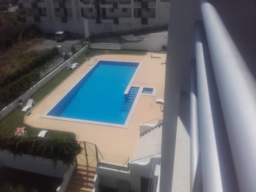 Área de piscina do Albufeira Inn com piscina retangular azul, deck bege e edifícios residenciais brancos
