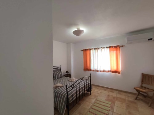 Quarto luminoso com camas de casal, cortinas laranja e azulejos de terracota na Villa Mulatinho em Olhos de Água, Portugal