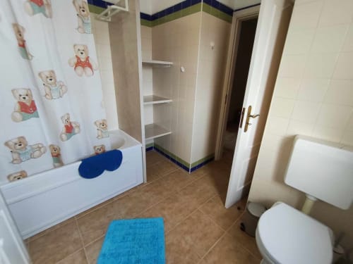 Casa de banho infantil em villa de Albufeira com cortina de chuveiro com urso de peluche, tapete azul, sanita e pavimento em azulejo.