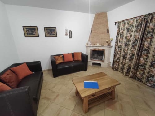 Espaçosa sala de estar com lareira, sofás de couro preto com almofadas laranja, mesa de café em madeira e cortinas estampadas