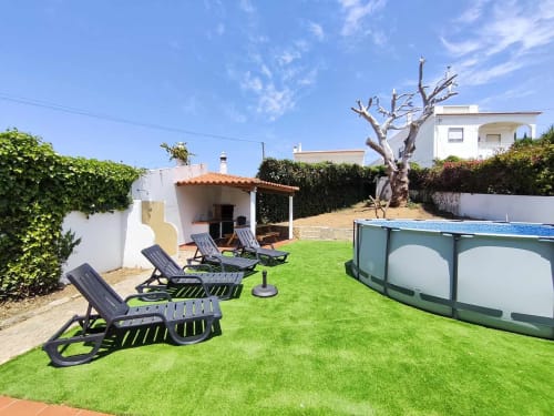 Jardim da Villa Mulatinho com espreguiçadeiras, piscina, árvore nua e casa branca em Olhos de Água, Portugal