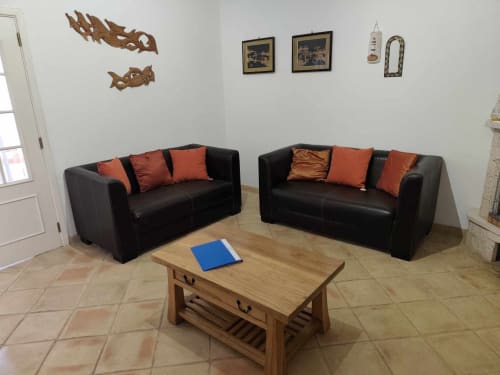 Moderna sala de estar com dois sofás de couro preto, almofadas laranja, mesa de centro em madeira e arte decorativa na parede em Albufeira