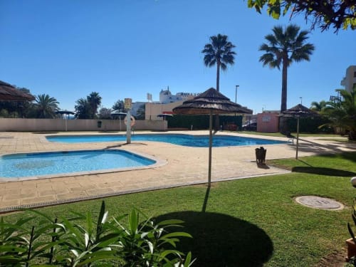 Área de piscina do Albufeira Inn com espreguiçadeiras, palmeiras e apartamentos do Bellavista Tenis Clube em Portugal