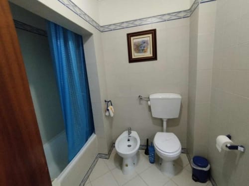Banheiro moderno no Albufeira Inn com sanitário, bidê e cortina de chuveiro azul