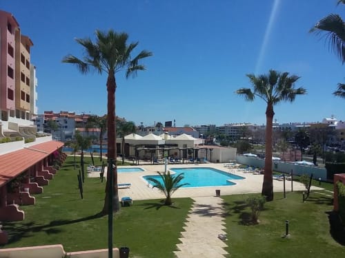 Vista do jardim do Albufeira Inn com piscina turquesa, palmeiras e edifício em terracota em Albufeira, Portugal