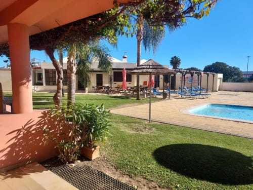 Vista do jardim do Albufeira Inn com piscina, palmeiras, espreguiçadeiras e edifício em terracota em Portugal