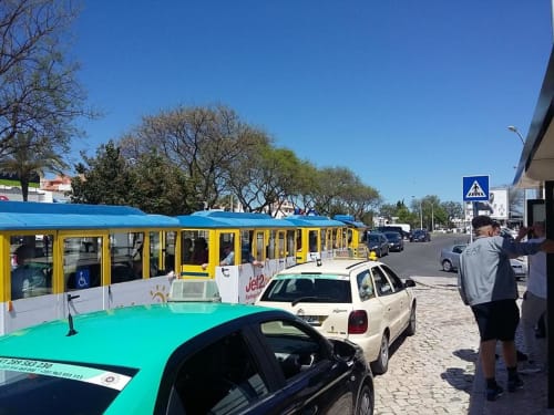Comboio turístico amarelo e táxis na Pousada Albufeira em Portugal com céu azul e árvores