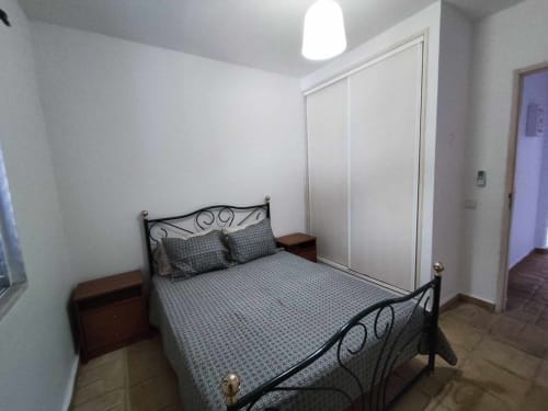 Quarto moderno na villa Albufeira Inn com cama de ferro preto, roupa de cama cinzenta, mesinha de cabeceira de madeira e guarda-roupa com espelho