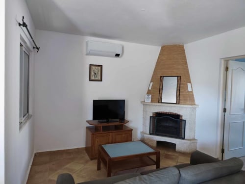 Sala de estar moderna com lareira, TV, móveis em madeira e piso em azulejo com vista para o jardim da villa em Albufeira