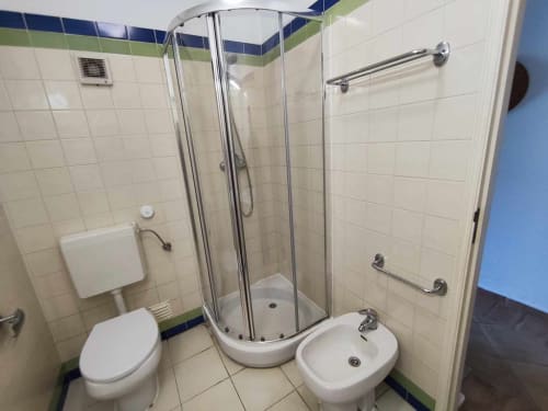 Banheiro moderno da villa Albufeira Inn com box de vidro curvo, vaso sanitário, bidê e paredes azulejadas com detalhes em azul