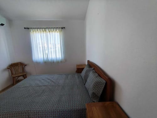 Quarto luminoso em moradia em Albufeira com cama de madeira, vista do jardim e paredes brancas minimalistas