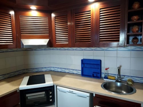Kitchenete moderna no apartamento Albufeira Inn com pia em aço inoxidável, micro-ondas, forno, escorredor azul e azulejos brancos