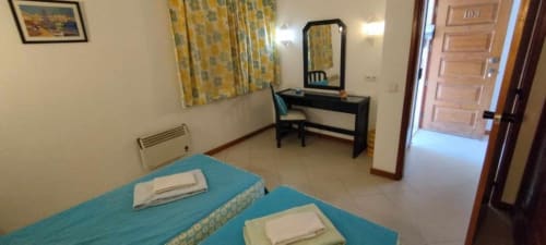 Quarto espaçoso no Albufeira Inn com camas de casal, penteadeira, espelho e piso em azulejo, com vista para o jardim.