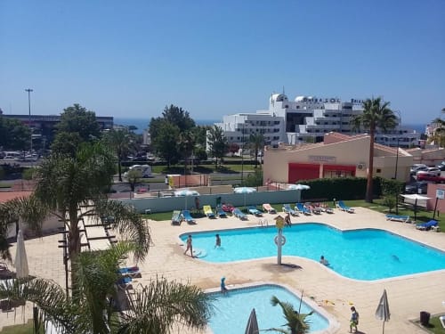Área de piscina do Albufeira Inn com duas piscinas, espreguiçadeiras, palmeiras e vista para o Mar Mediterrâneo