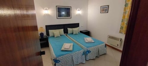 Quarto moderno na Albufeira Inn com camas individuais, roupa de cama azul, cabeceira preta, arandelas de parede e vistas para o jardim