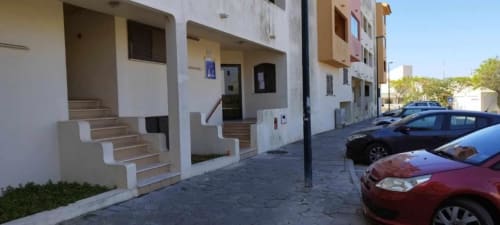Edifício de apartamentos em Albufeira com fachada branca, escadas de entrada, carros estacionados e vista para o jardim em Portugal