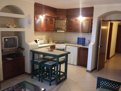Cozinha e área de refeições modernas no apartamento Albufeira Inn com armários em madeira, fogão, eletrodomésticos brancos e mesa de jantar verde-azulada.
