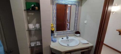 Banheiro moderno com lavatório circular branco, espelho grande, prateleiras e paredes revestidas no apartamento Albufeira Inn